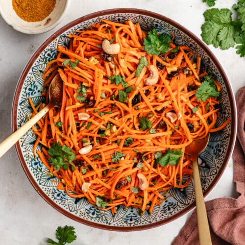 The carrot salad in a serving bowl topped with fresh herbs and chopped cashews.