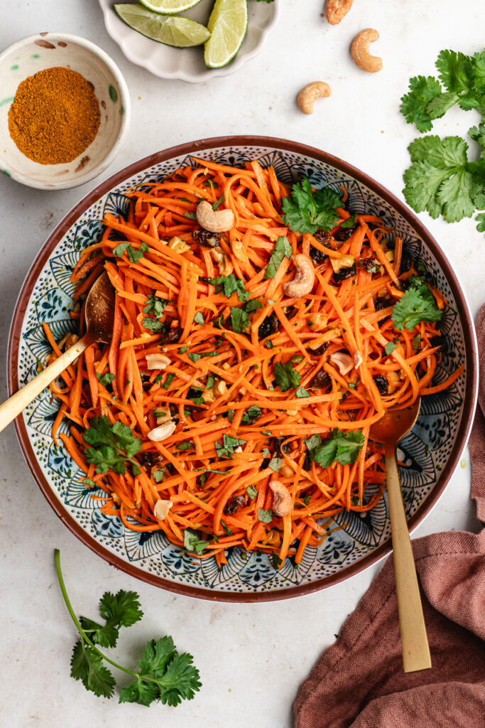The carrot salad in a serving bowl topped with fresh herbs and chopped cashews.