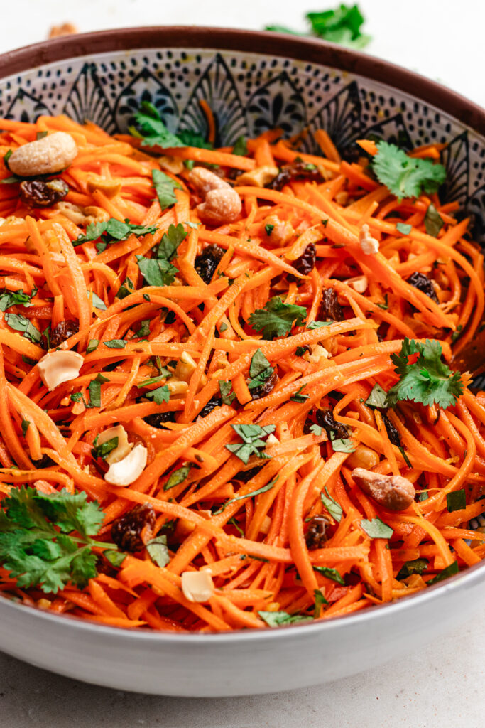 The carrot salad in a serving bowl topped with fresh herbs and chopped cashews.