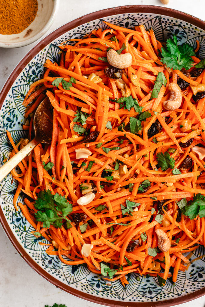 The carrot salad in a serving bowl topped with fresh herbs and chopped cashews.