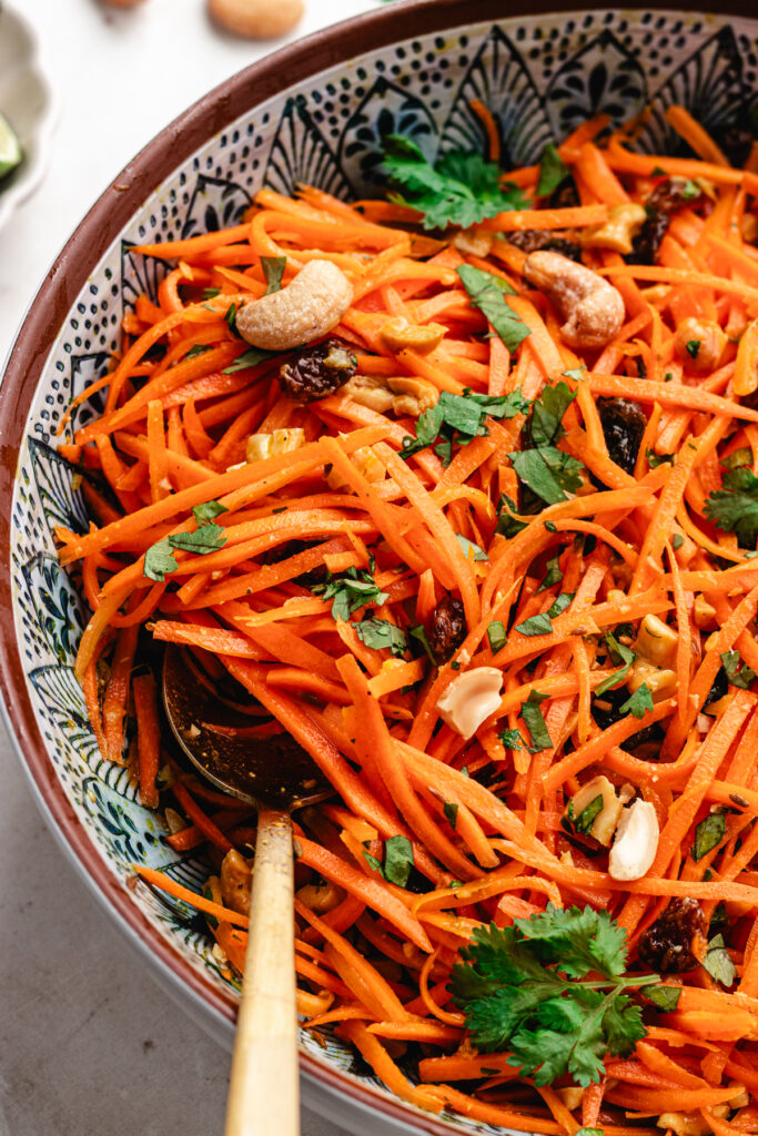 The carrot salad in a serving bowl topped with fresh herbs and chopped cashews.