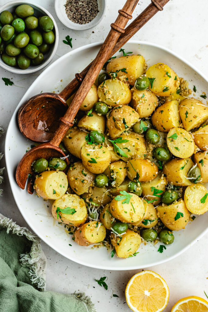 The potato salad in a bowl topped with herbs and green olives.