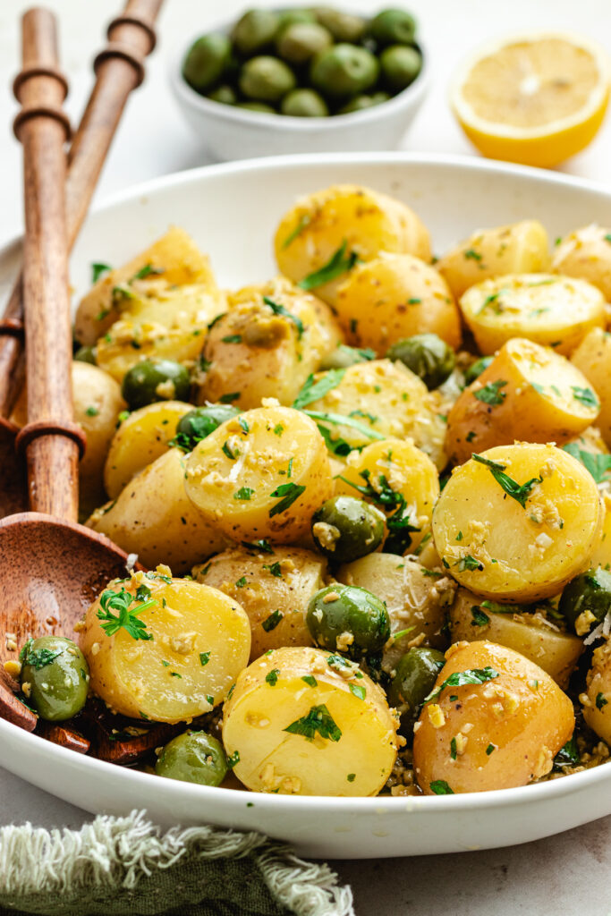 The potato salad in a bowl topped with herbs and green olives.