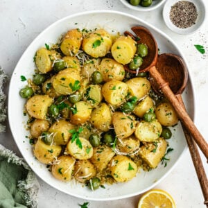 The potato salad in a bowl topped with herbs and green olives.