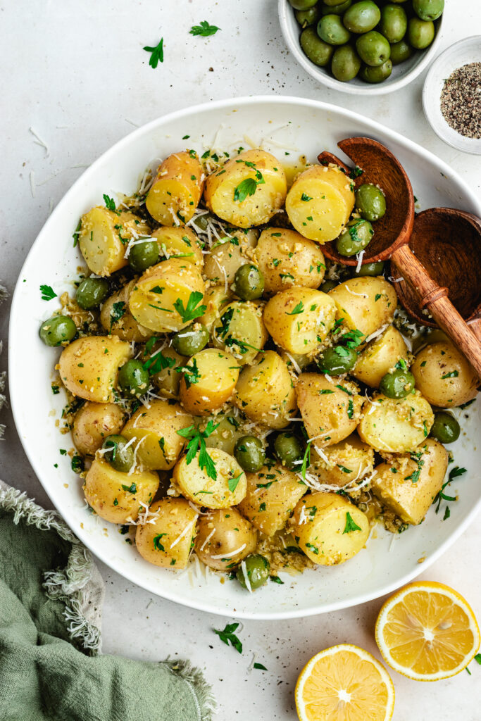 The potato salad in a bowl topped with herbs and green olives.
