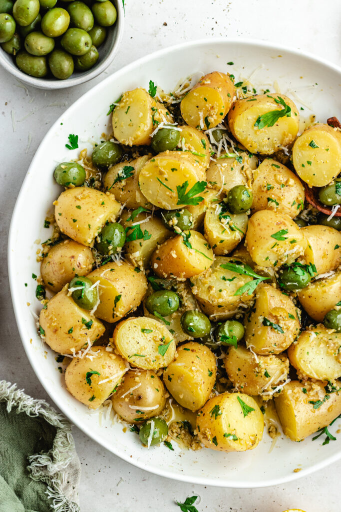 The potato salad in a bowl topped with herbs and green olives.