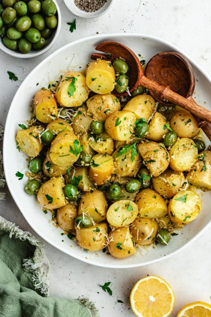 The potato salad in a bowl topped with herbs and green olives.