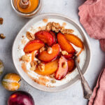 The roasted plums in a bowl with greek yoghurt and chopped nuts.