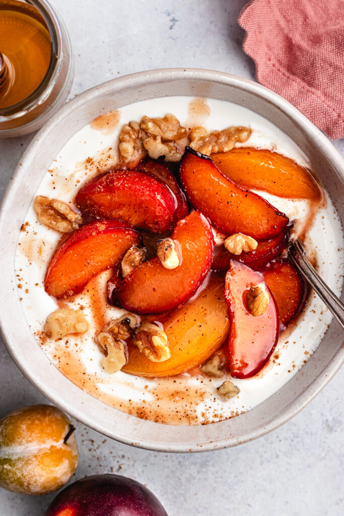 The roasted plums in a bowl with greek yoghurt and chopped nuts.