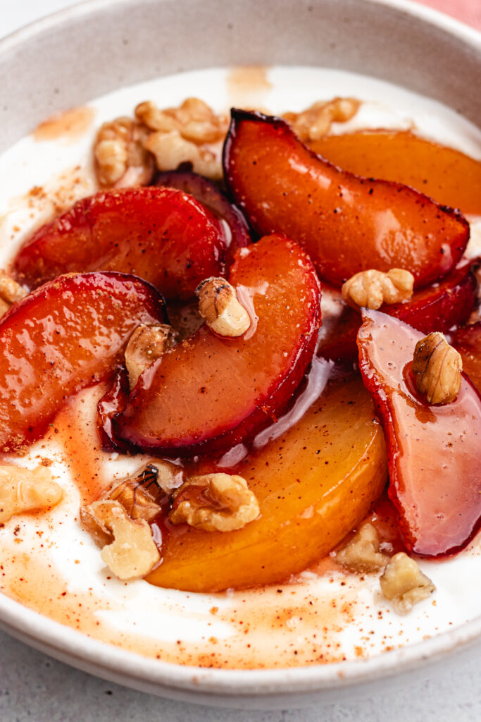 The roasted plums in a bowl with greek yoghurt and chopped nuts.