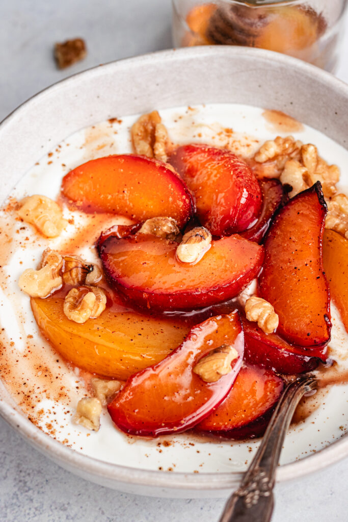 The roasted plums in a bowl with greek yoghurt and chopped nuts.