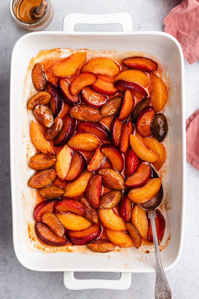 The roasted plums in the baking dish with a spoon.