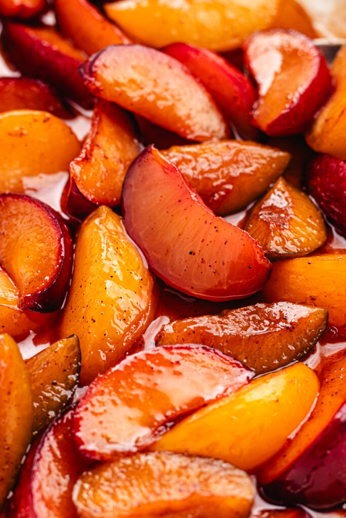 The roasted plums in the baking dish with a spoon.