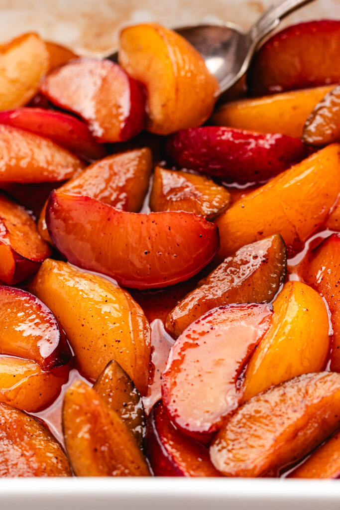 The roasted plums in the baking dish with a spoon.