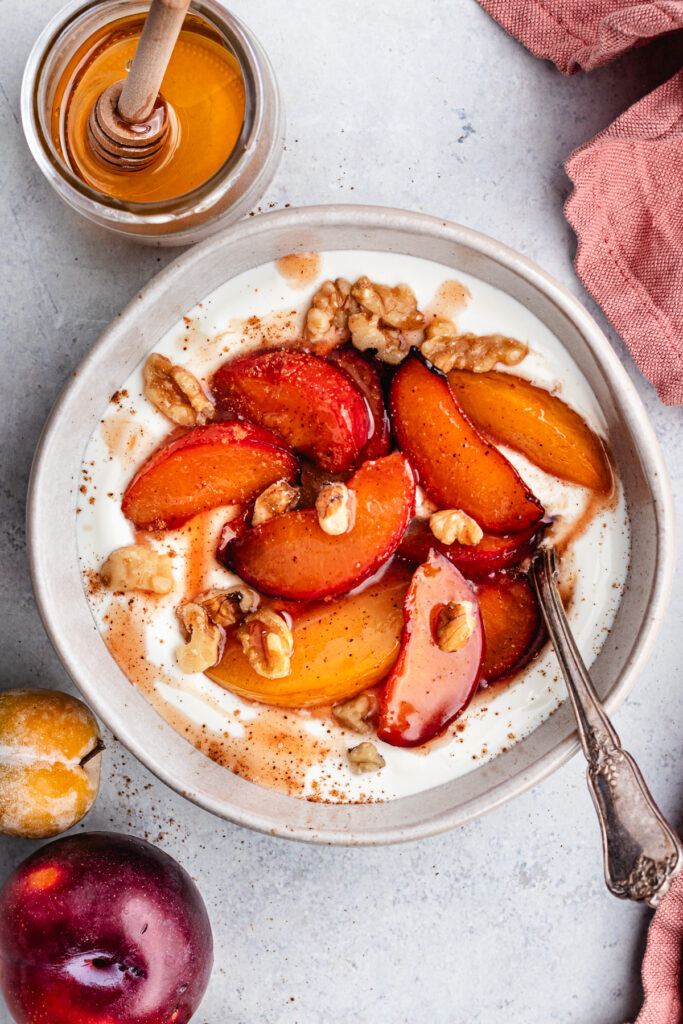 The roasted plums in a bowl with greek yoghurt and chopped nuts.
