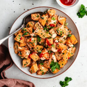 The potato salad on a bowl topped with sauce and fresh herbs.