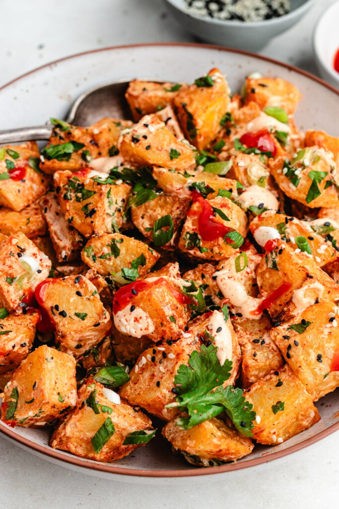 The potato salad on a bowl topped with sauce and fresh herbs.