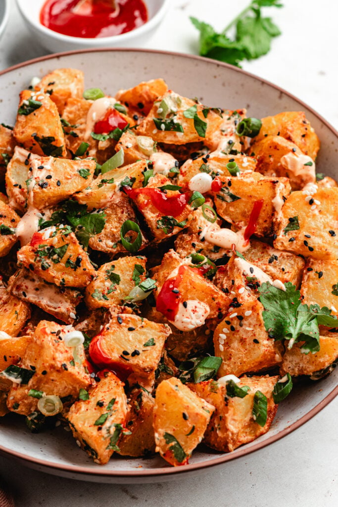 The potato salad on a bowl topped with sauce and fresh herbs.