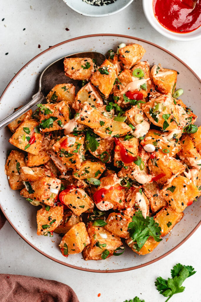 The potato salad on a bowl topped with sauce and fresh herbs. 