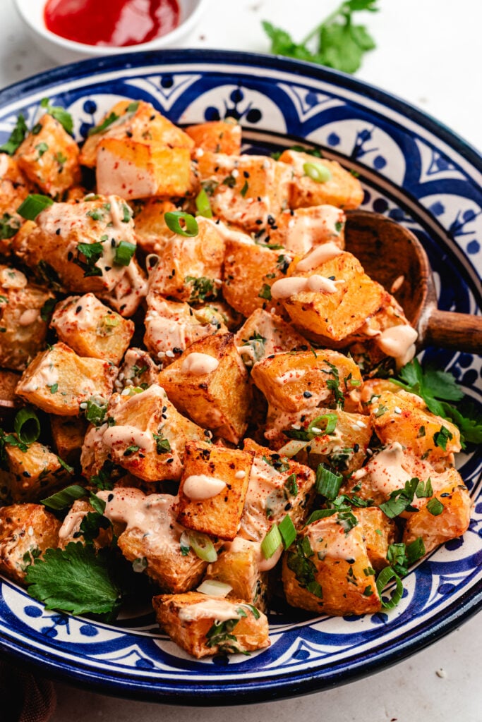 The potato salad on a bowl topped with sauce and fresh herbs.