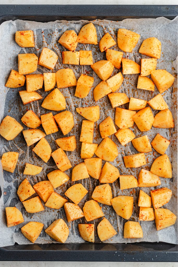 The potatoes with oil and spices on a sheet pan.