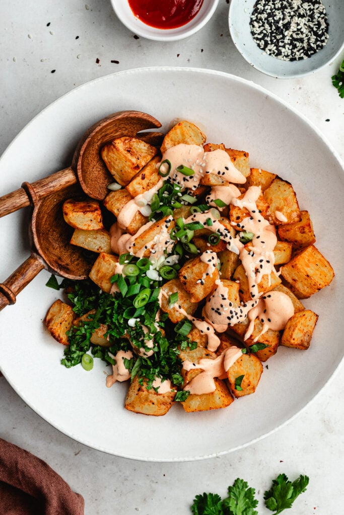 The potatoes topped with the sauce, herbs, green onions and sesame seeds.
