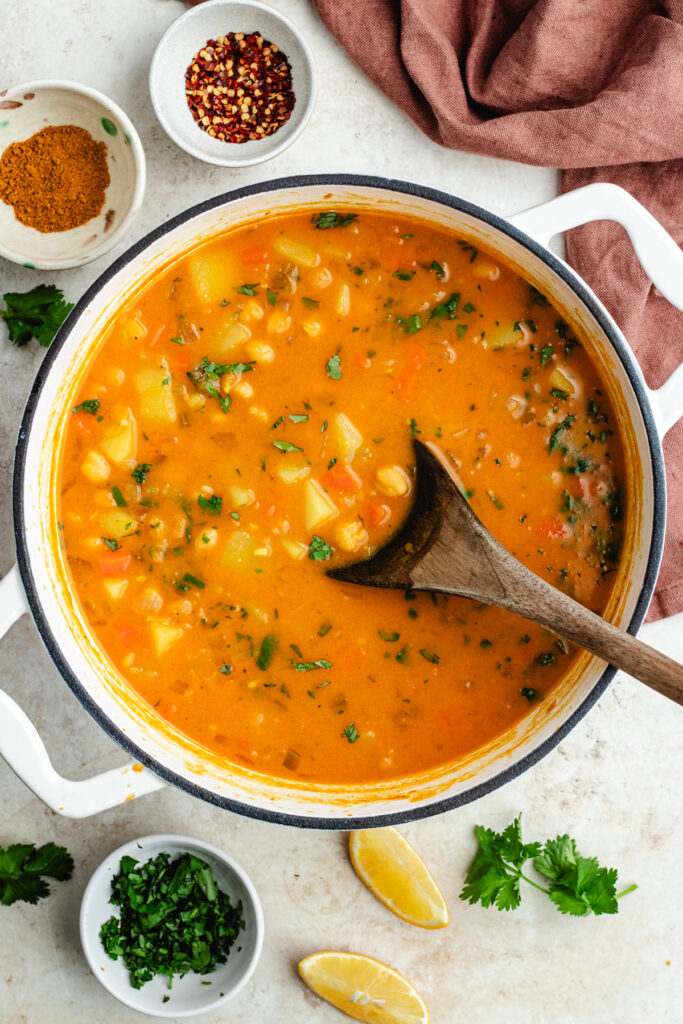 The soup in the pot with a spoon topped with cilantro and lemon juice.