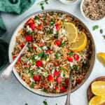 The rice salad in a salad bowl topped with fresh herbs and lemon slices.