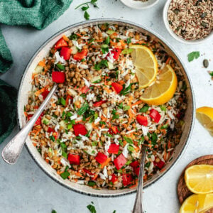 The rice salad in a salad bowl topped with fresh herbs and lemon slices.
