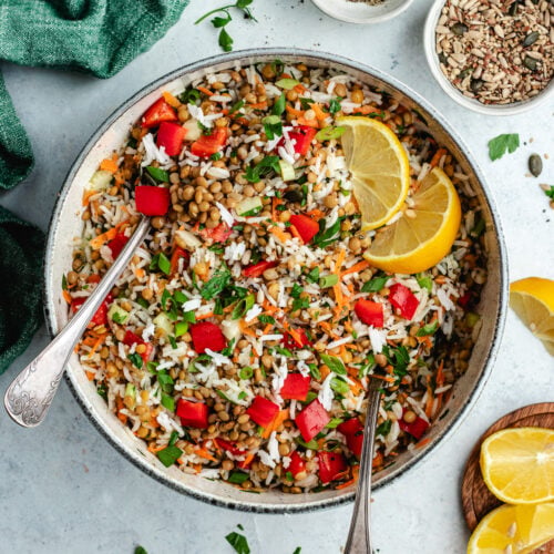 The rice salad in a salad bowl topped with fresh herbs and lemon slices.
