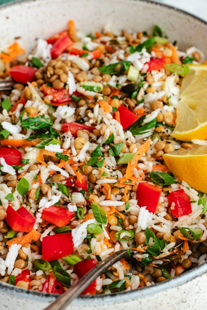 The rice salad in a salad bowl topped with fresh herbs and lemon slices.