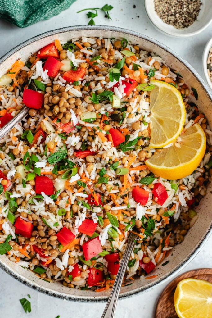 The rice salad in a salad bowl topped with fresh herbs and lemon slices.